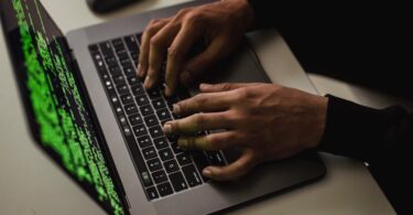 crop cyber spy hacking system while typing on laptop